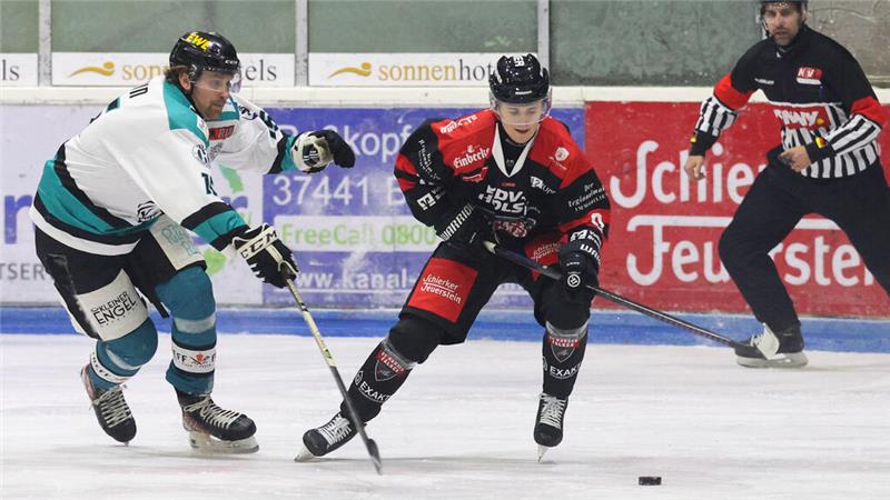 Zwei Eishockeyspieler in Aktion auf dem Eis, einer in weiß-grünem Trikot, der andere in schwarz-rotem Trikot, mit Schiedsrichter im Hintergrund