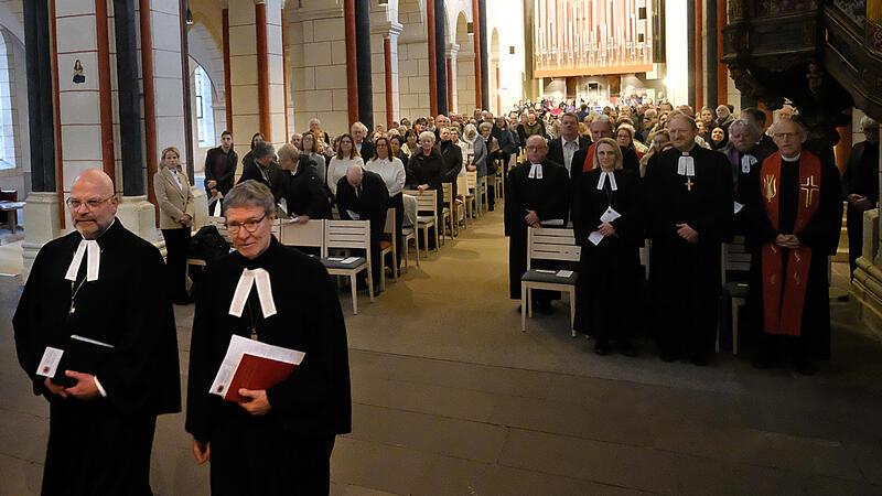 Zwei Männer in Kirchenroben stehen vor einem mit Menschen voll besetzten Kirchenschiff.