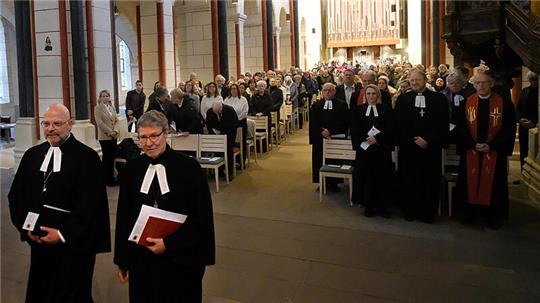 Zwei Männer in Kirchenroben stehen vor einem mit Menschen voll besetzten Kirchenschiff.
