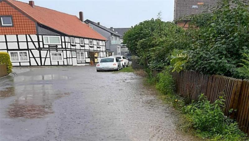 Dorfstraße mit Fachwerkhäusern links und dichtem Grün rechts bei nassem Wetter