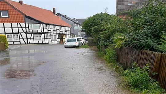 Dorfstraße mit Fachwerkhäusern links und dichtem Grün rechts bei nassem Wetter