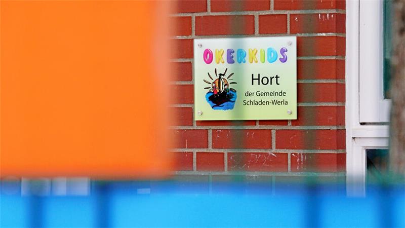 Schild mit bunter Aufschrift 'OKERKIDS' und Text 'Hort der Gemeinde Schladen-Werla' an roter Backsteinwand neben weißem Fensterrahmen