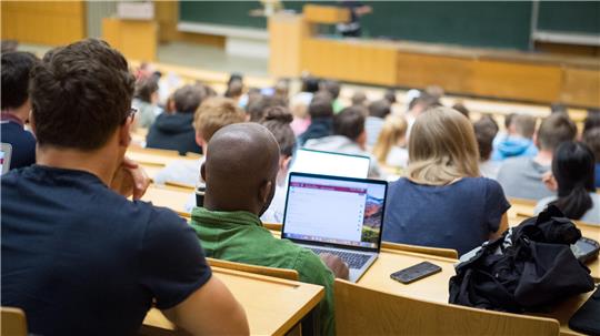 Studierende sitzen in einem Hörsaal und blicken auf einen Laptop mit geöffnetem Textdokument