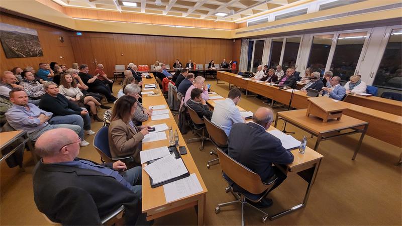 Das Bild zeigt einen Sitzungssaal voller Menschen, die an Tischen und auf Stühlen sitzen.