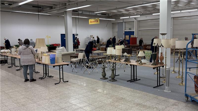 Großer Raum mit mehreren Tischen, auf denen verschiedene Lampen und Leuchten stehen, mehrere Personen im Hintergrund.