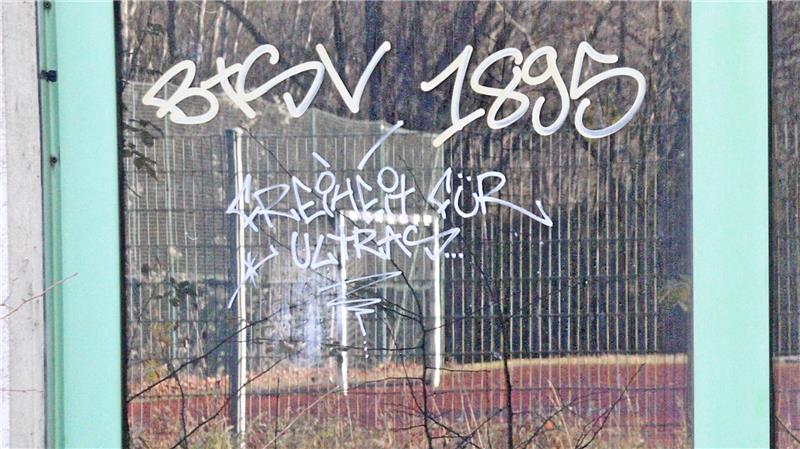 Schmierereien an der Sporthalle Liebenburg, in der Scheibe spiegelt sich der Sportplatz neben der Halle.