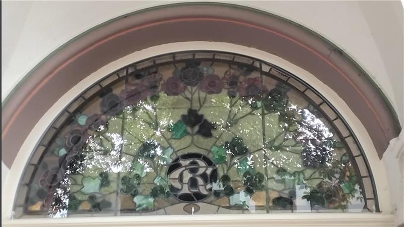 Zur Bummelallee hin zeigt ein Oberlichtbleiglasfenster, auf dem die Initialen von Bauherr Carl Rautmann verewigt worden sind.