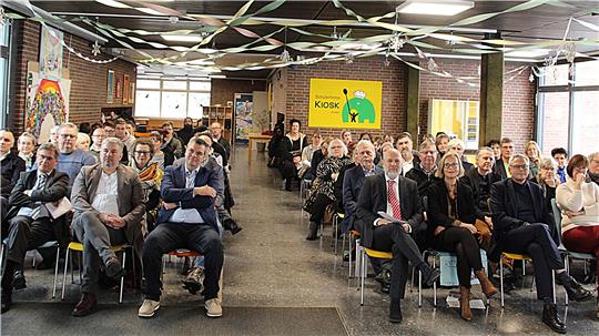 Mehrere Menschen sitzen auf Stühlen in einem geschmückten Saal.