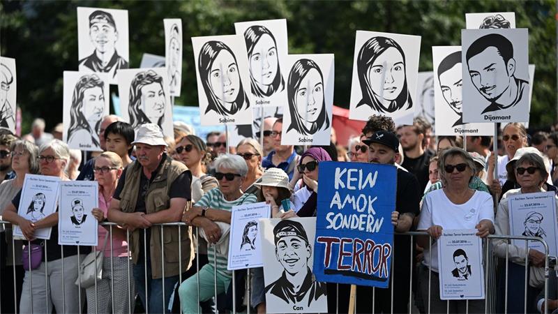 Zuschauer des Gedenkaktes der Landeshauptstadt München anlässlich des 10. Jahrestags des Attentats am Olympia-Einkaufszentrum halten Plakate mit Portraits der Opfer.