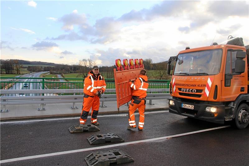 Zwei Arbeiter tragen die Sperrbaken weg, sodass die Brücke über die B 82 nun frei befahrbar ist.  Foto: Leifeld