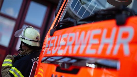 Ein Feuerwehrmann steht in voller Montur vor einem Feuerwehrfahrzeug.