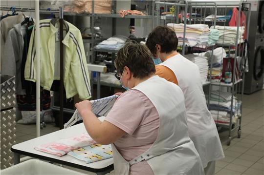 Zwei Frauen arbeiten in der Wäscherei der Lebenshilfe Gera e.V und legen dort Wäsche zusammen.