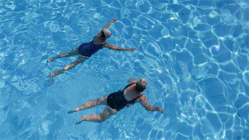 Zwei Frauen erfrischen sich in einem Außenbecken eines Schwimmbads. 