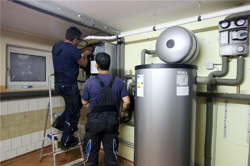 Blick in den Keller: Wie wird die Heizung klimaneutral? Zwei Handwerker stellen eine gerade installierte Wärmepumpe im Keller einer Doppelhaushälfte ein.