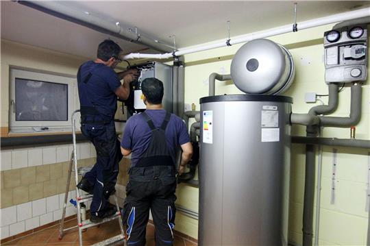 Zwei Handwerker stellen eine gerade installierte Wärmepumpe im Keller einer Doppelhaushälfte ein.