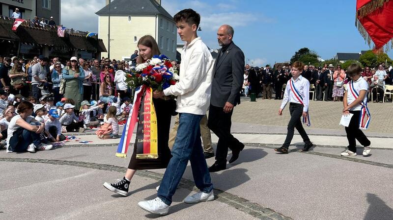 Liebenburger nehmen am D-Day-Gedenken in der Normandie teil Zwei Jugendliche der Delegation aus dem Landkreis Goslar schreiten mit Liebenburgs Gemeindejugendpfleger Gerold König zur Kranzniederlegung.