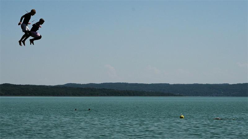 Zwei Jungen in Neoprenanzügen springen vom Sprungturm im Strandbad am Ammersee.