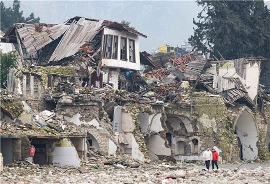 Zwei Männer gehen an einer völlig zerstörten Häuserzeile in Antakya vorbei. Im Zentrum der Stadt waren bei dem Beben vor einem Jahr unzählige Häuser zerstört oder beschädigt worden.