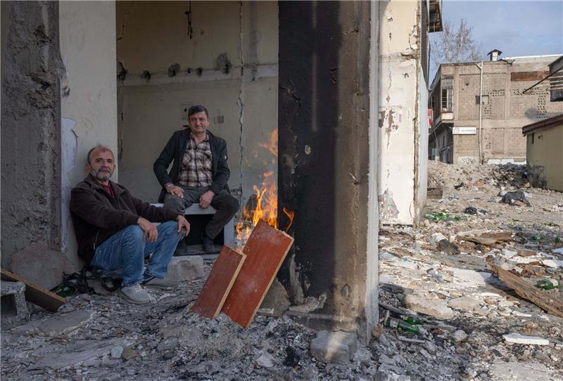 Knapp ein Jahr nach Beben: Erdoğan besucht Provinz Hatay Zwei Männer wärmen sich in den Trümmern eines zerstörten Hauses in Kahramanmaras an einem Feuer. Im Zentrum der Stadt waren bei dem Beben vor einem Jahr unzählige Häuser zerstört oder beschädigt worden.