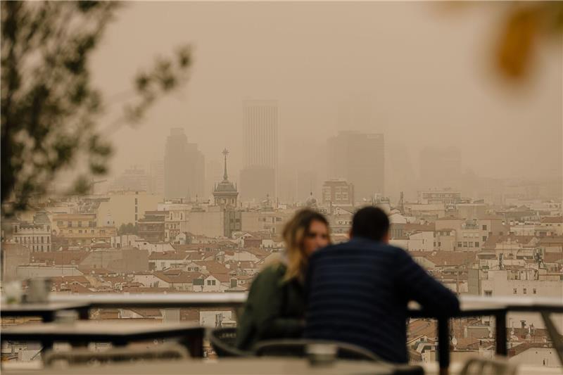 Sahara-Staub auf Autos und Fenstern möglich Zwei Menschen sitzen in Madrid auf einer Terrasse, während eine Wolke mit Sahara-Staub über die spanische Hauptstadt zieht. Die typische Auswirkung von Sahara-Staub ist ein roter oder orangener Himmel. (Archivbild)