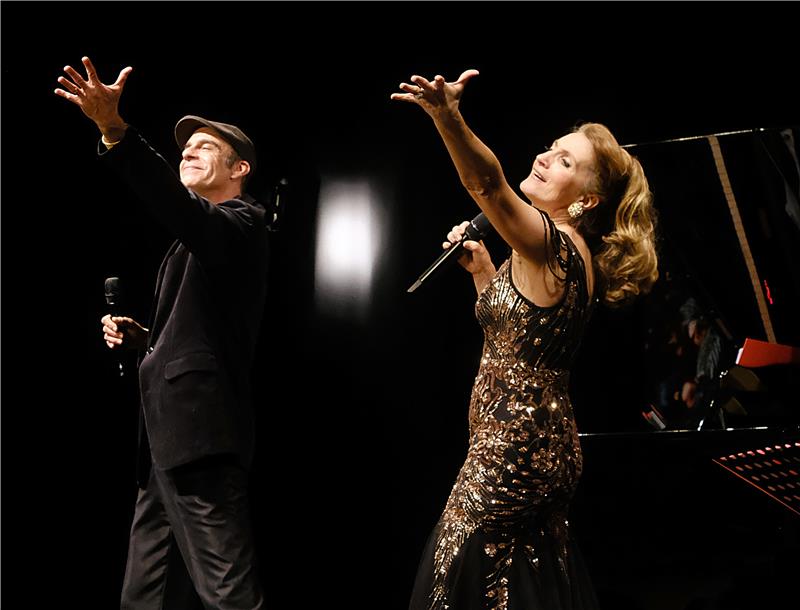 Ein Mann und eine Frau in festlicher Kleidung heben die Arme zu einer gemeinsamen Choreografie.