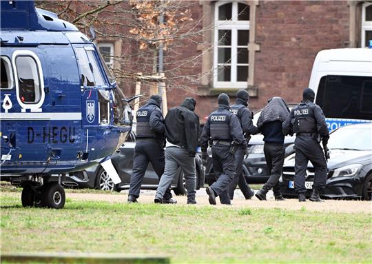 Zwei Personen werden von Polizisten von einem Hubschrauber zu einem Auto geführt.