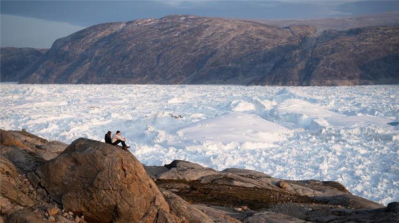 Zwei Studenten der New York University sitzen auf einem Felsen mit Blick auf den grönländischen Helheim-Gletscher. 
