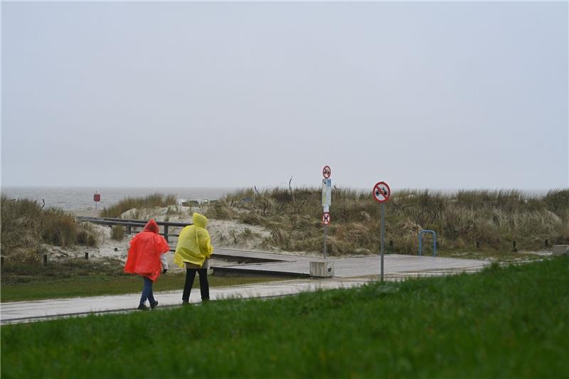 Küste bereit für Saisonstar: Strandkörbe kommen ins Freie Zwei Tagesgäste laufen bei nassem Wetter in Regenjacken an der Starndpromenade entlang.