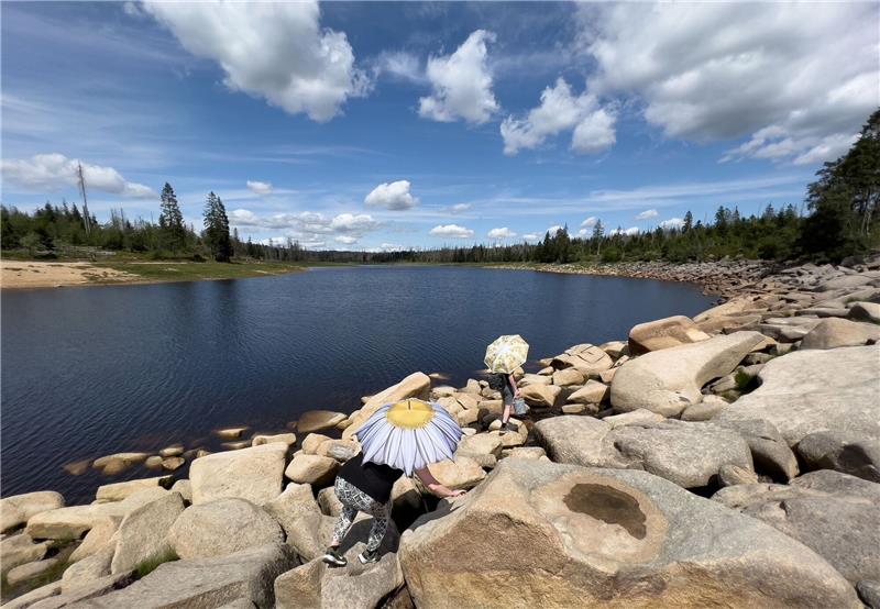 Zwei Touristen klettern mit Regenschirmen als Sonnenschutz über Steine am Ostufer vom Oderteich im Nationalpark Harz.