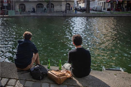 Zwei junge Männer trinken am Ufer des Kanals Saint-Martin gemeinsam Bier.