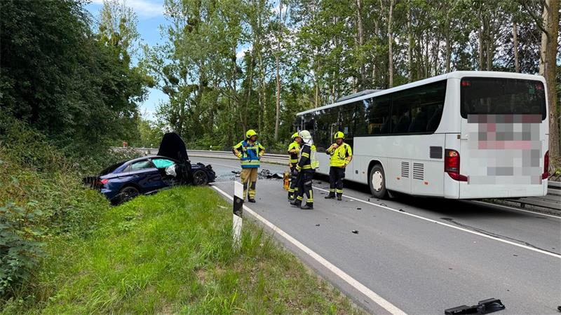 Ein beschädigtes Auto liegt im Graben, während ein ebenfalls beschädigter Bus auf der Straße steht. 