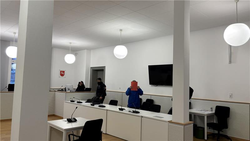 Innenraum mit mehreren Personen an einem langen, weißen Konferenztisch, an der Wand ein großer Flachbildschirm und runde Deckenleuchten.