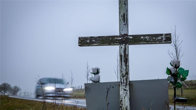 in Auto fährt auf einer Landstraße an einem hölzernen Kreuz vorbei, welches zur Erinnerung an ein Unfallopfer aufgestellt wurde.